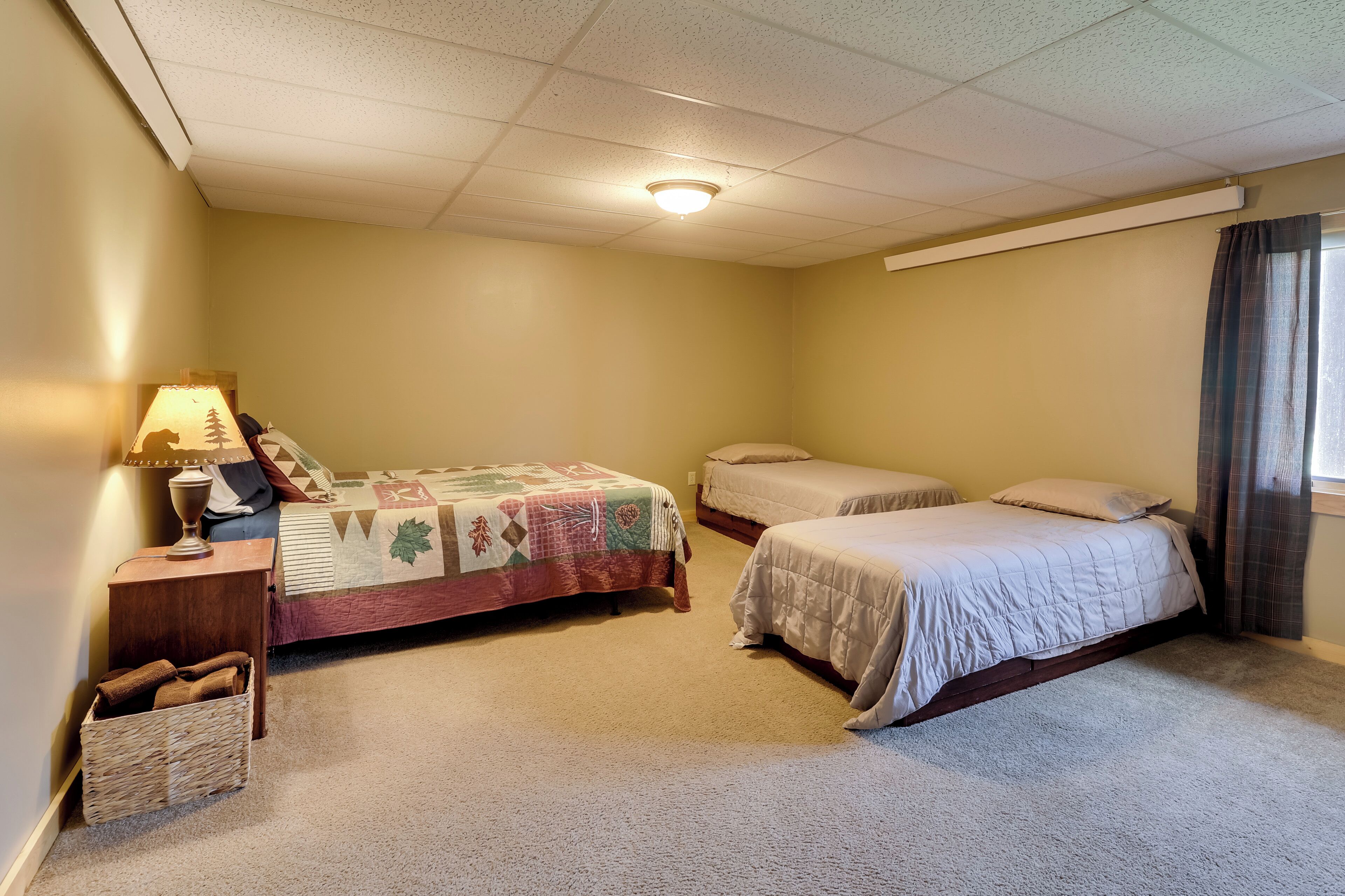 A bedroom with two beds, a nightstand, a lamp, and a small basket.