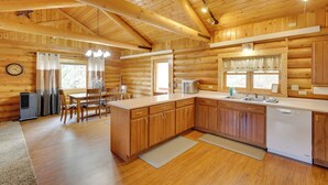 A log cabin with a wooden interior, including a kitchen with a sink, stove, and dining area with chairs and a table.