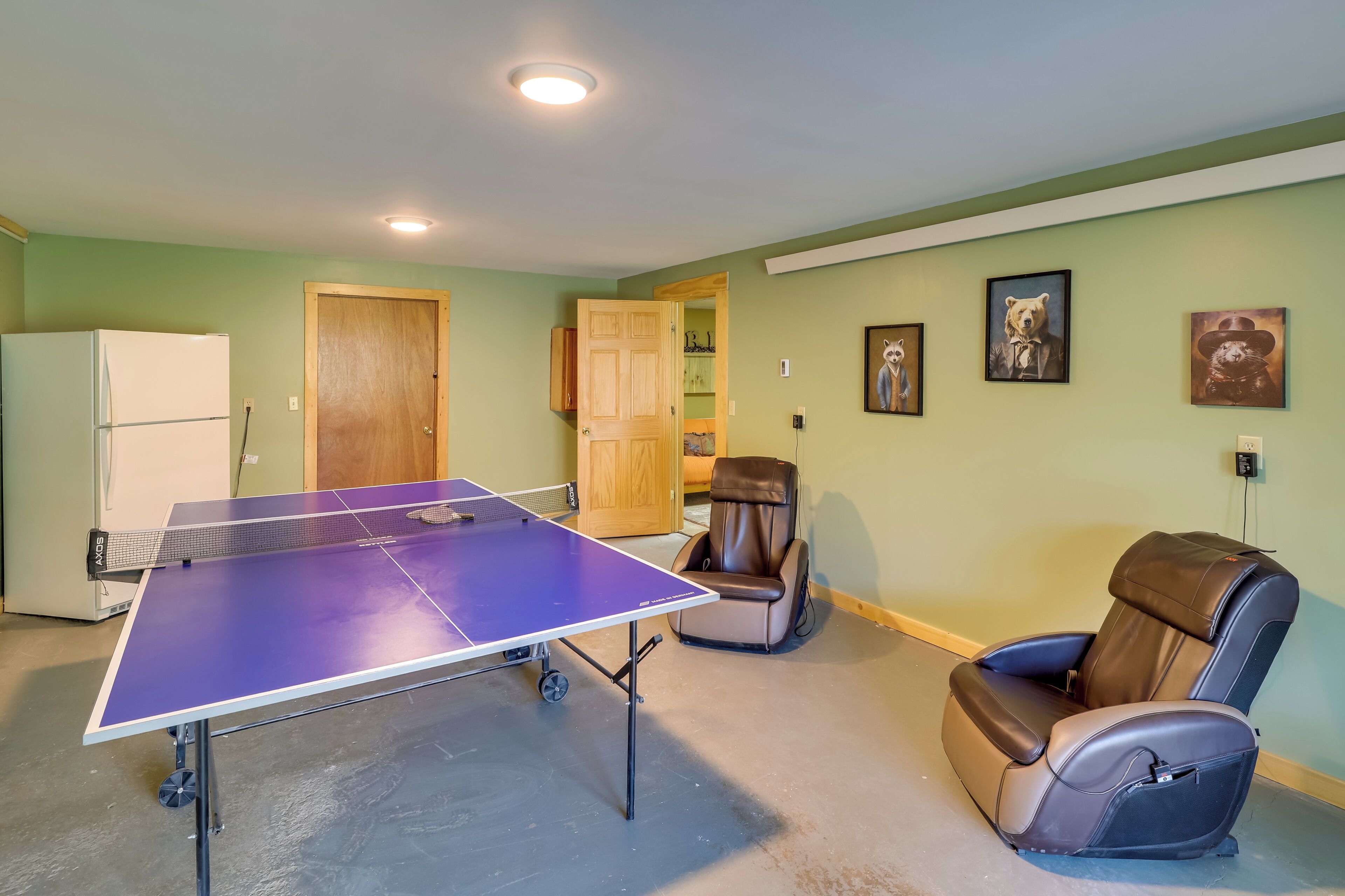 A room with a ping pong table, a massage chair, and a refrigerator.