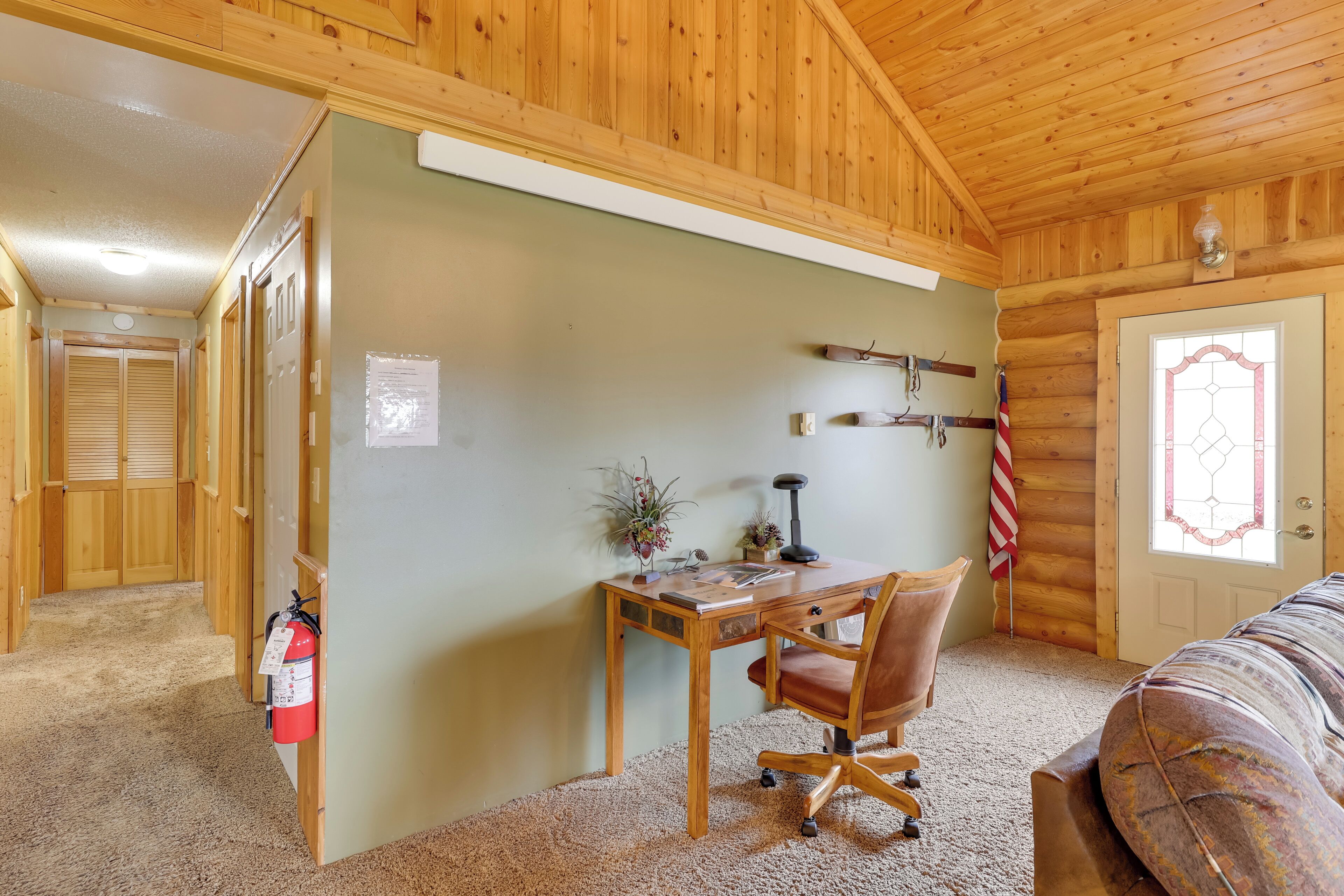 A wooden cabin interior with a desk, chair, and a fire extinguisher.