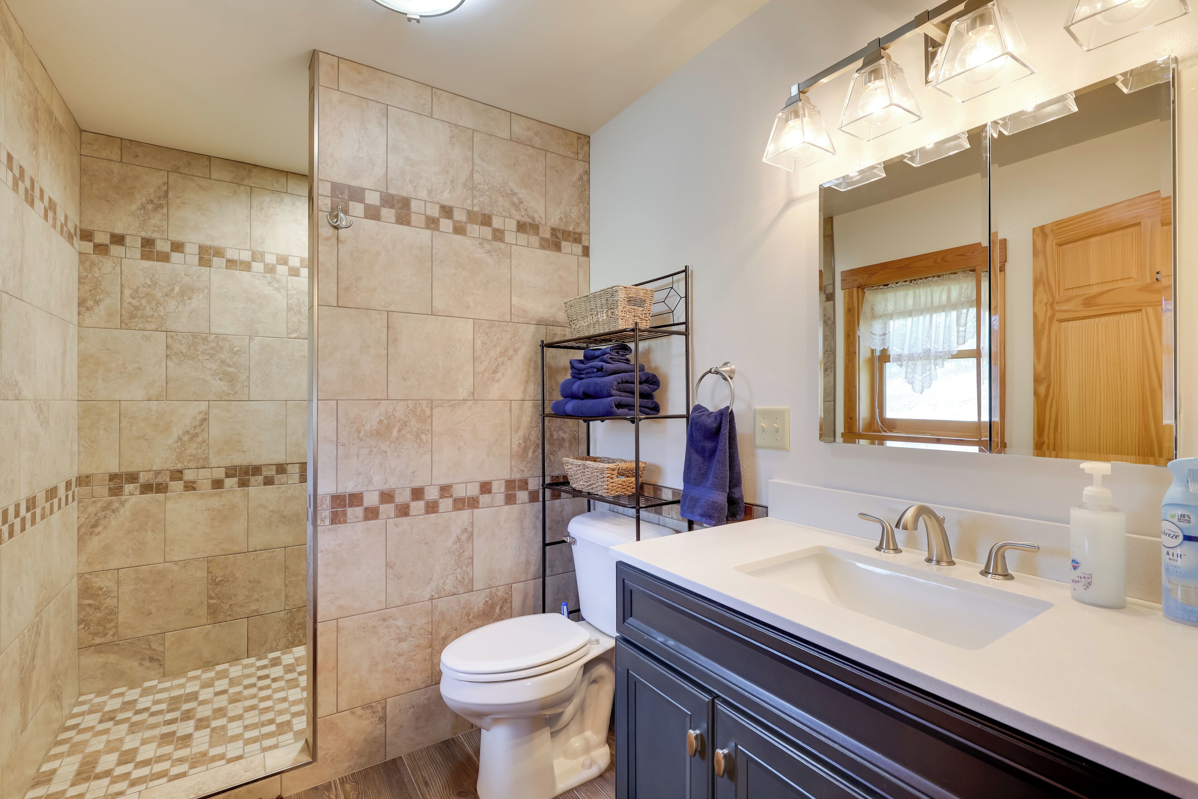 A bathroom with a shower, toilet, sink, and a shelf with towels.