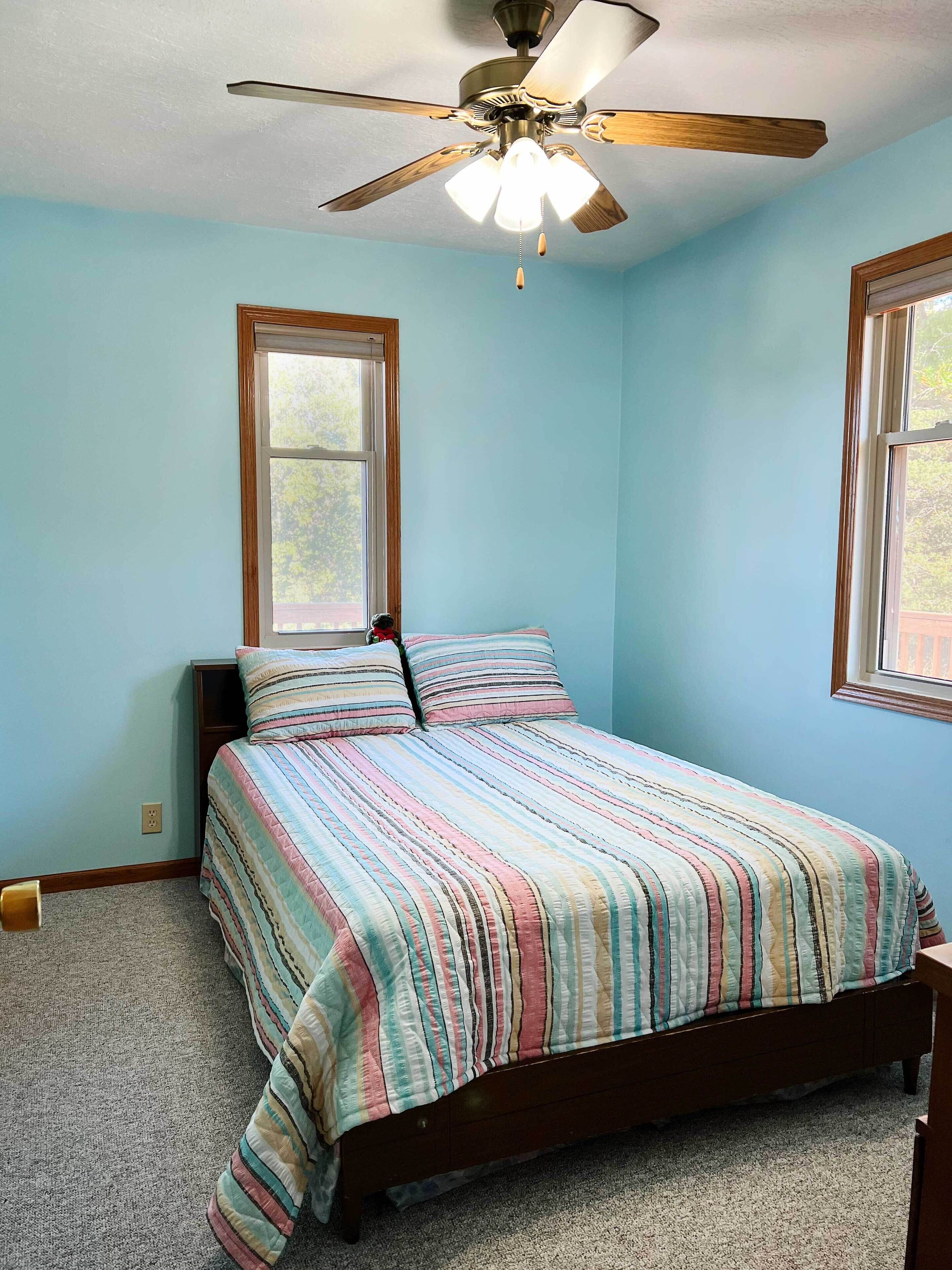 A bedroom with a bed, a ceiling fan, and two windows.