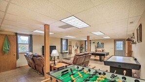 Une pièce avec une table de baby-foot, des fauteuils en cuir, une table de billard et une fenêtre avec des rideaux.