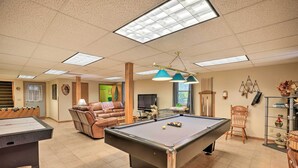 Une table de billard, une table de baby-foot et un fauteuil inclinable dans une pièce bien éclairée, équipée d’une télévision et agrémentée d’objets décoratifs.
