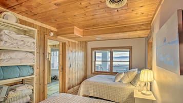 A wooden cabin bedroom with two beds, a window with a view, and a shelf with folded towels.