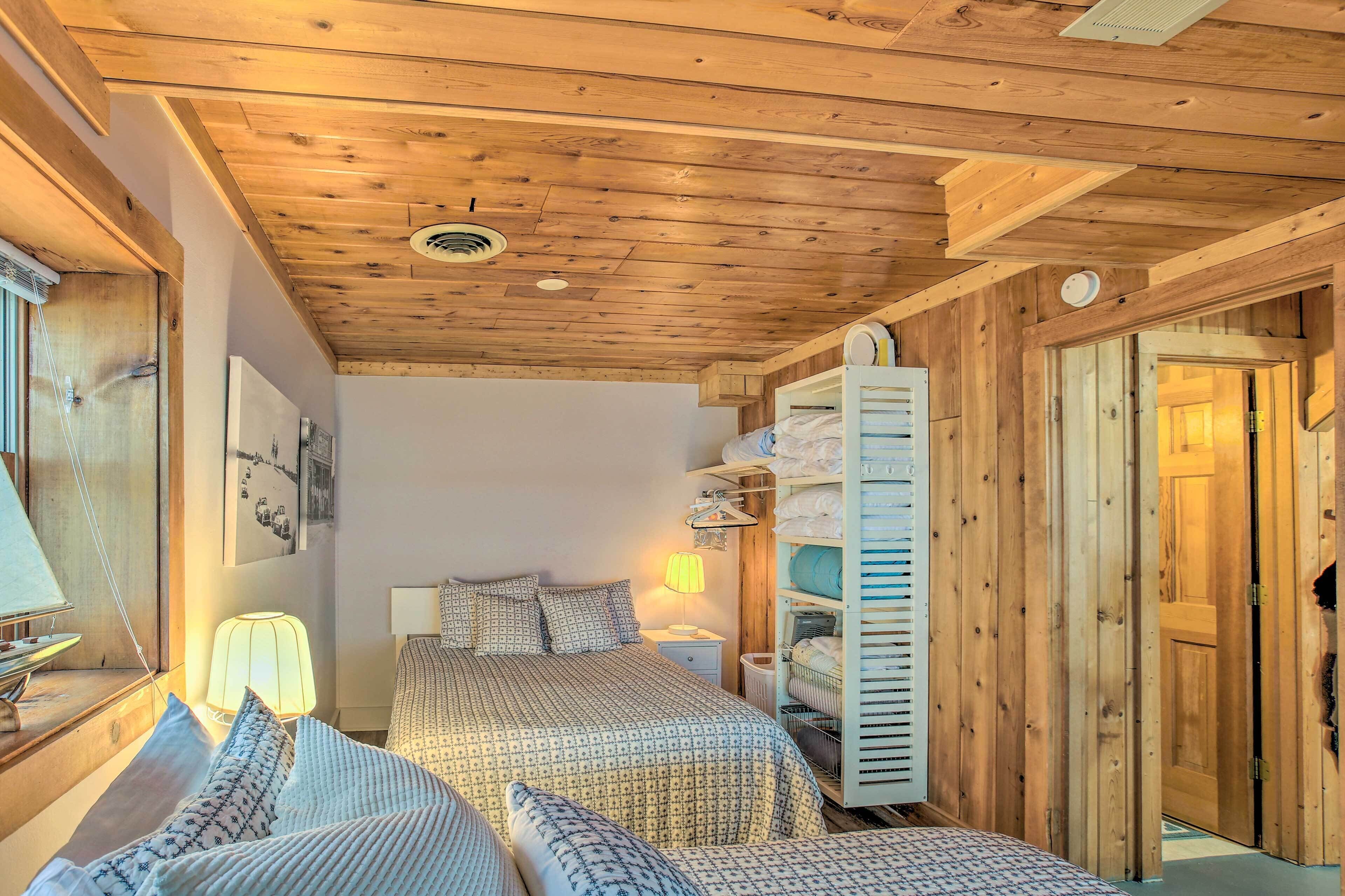 A cozy bedroom with a wooden ceiling, a bed with patterned bedding, a bedside table with a lamp, and a wardrobe with hanging space.