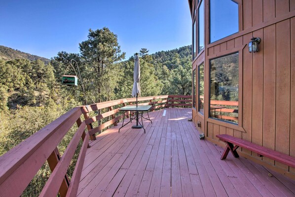 A wooden deck with a table and bench, overlooking a forested area.