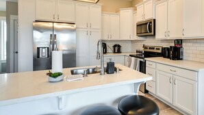 Una cocina moderna con armarios blancos, electrodomésticos de acero inoxidable y una isla central con taburetes.
