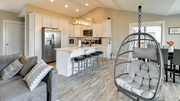 Una cocina moderna con armarios blancos, una isla central con taburetes de bar, una silla colgante y un comedor con mesa y sillas.