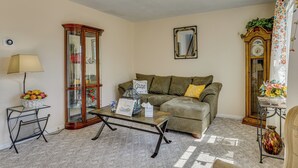 A living room with a sofa, a glass cabinet, a lamp, a mirror, and a clock on the wall. - Jacksonville Getaway ~ 4 Mi to Downtown! (Jacksonville)