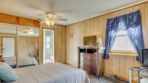 Een slaapkamer met een bed, een dressoir, een televisie en een raam met gordijnen.