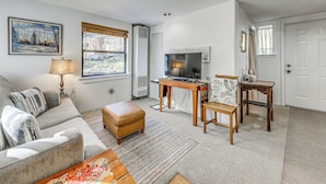A living room with a sofa, ottoman, and a coffee table. There is a TV on a stand, a small table, and a chair. - Ruidoso Cabin w/ Decks ~ 1 Mi to Downtown! (Ruidoso)