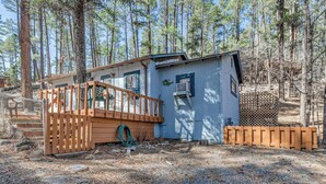 A cabin with a wooden deck, a small attached structure, and a fenced yard surrounded by tall pine trees. - Ruidoso Cabin w/ Decks ~ 1 Mi to Downtown! (Ruidoso)