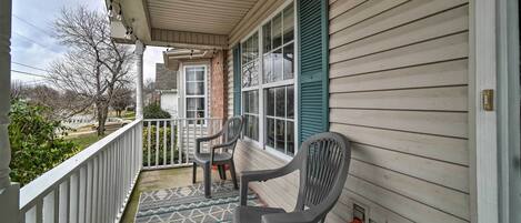 A porch with two chairs, a patterned rug, and a view of the street.