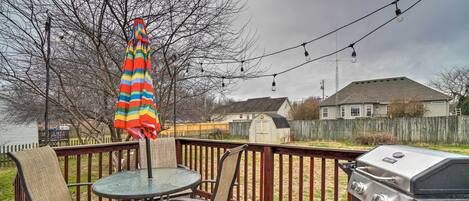 A deck with a grill, chairs, and an umbrella.