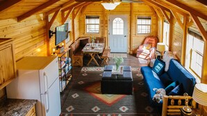 A cozy log cabin interior with a dining area, a living room with a blue sofa, and a kitchen with a refrigerator. - Paradise Valley Cabin by Chico & Yellowstone Park! (Livingston)