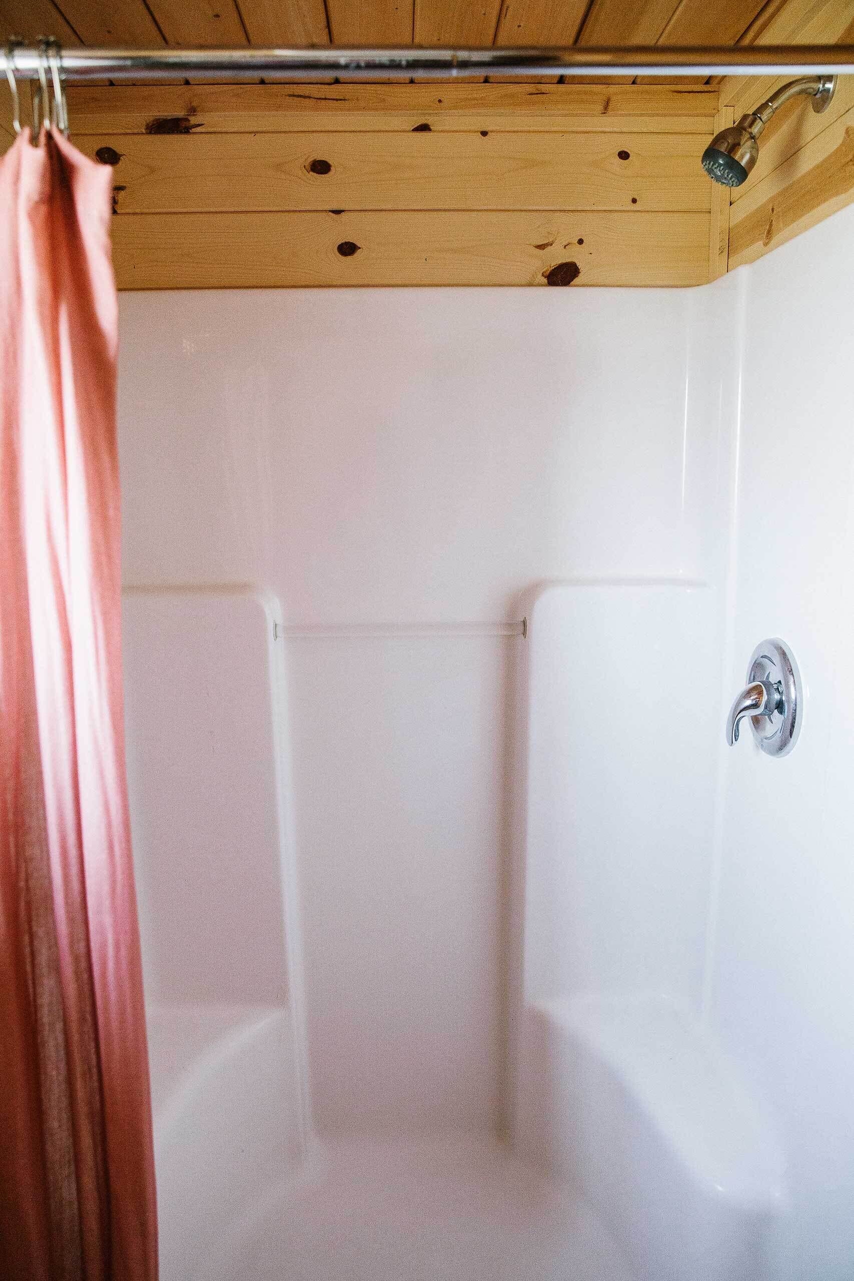 Een douchegedeelte met een houten plafond, witte wanden en een douchegordijn.
