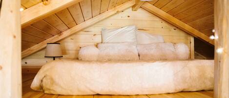 A cozy attic bedroom with a wooden ceiling, a bed with fluffy bedding, and a bedside lamp.