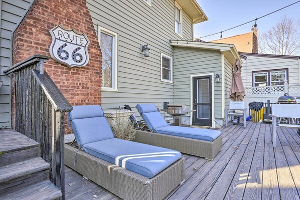 A deck with two wicker lounge chairs and a brick wall with a Route 66 sign. - Classic Teaneck Colonial Home With A Modern Touch (Teaneck)