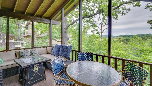 A covered outdoor seating area with a glass table and wicker chairs, overlooking a lush green landscape.