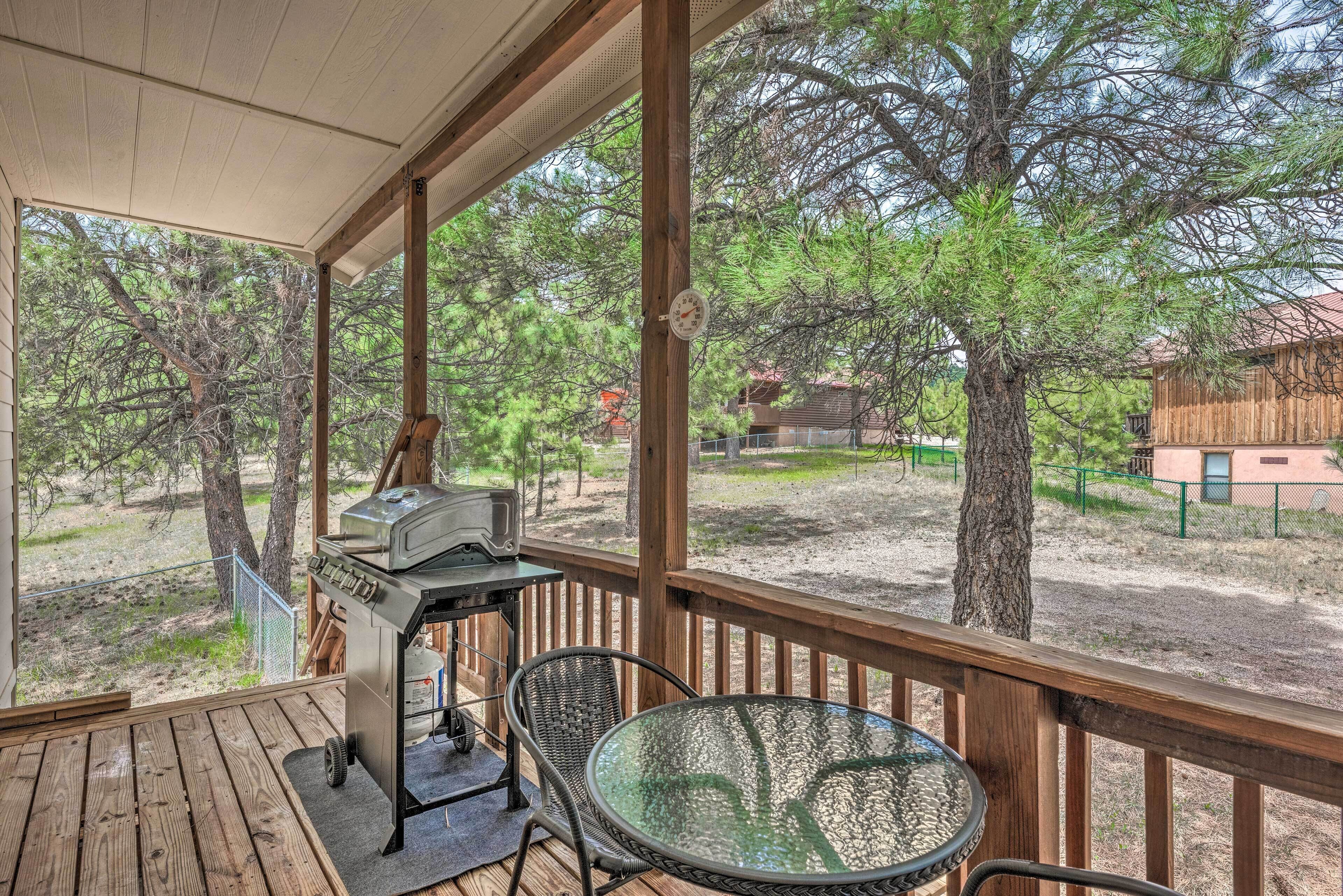 Un espace extérieur abrité, équipé d’un barbecue, de chaises et offrant une vue sur les arbres et les bâtiments.