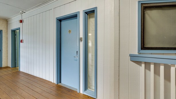 Un pasillo con suelo de madera, puertas azules y un ventanal con marco blanco.