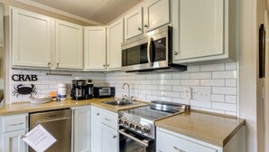 Una cocina con gabinetes blancos, un microondas de acero inoxidable, una cafetera y un lavavajillas.