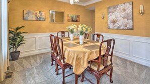 Comedor con una mesa dispuesta para seis personas, rodeada de sillas de madera, una araña y obras de arte en las paredes.