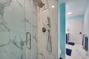 A bathroom with marble walls, a shower, a toilet, and a door leading to another room.