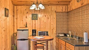 Una cocina compacta con paredes de madera, una mesa redonda, un refrigerador, un microondas y un lavabo.