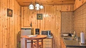 Una cocina compacta con paredes de madera, un refrigerador, un microondas, un lavamanos y una pequeña mesa de comedor.