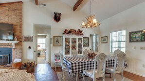 A dining area with a checkered tablecloth, white chairs, a chandelier, and a bear head mounted on the wall. - Nantahala Lake Family Home w/ Private Dock & Views (Topton)
