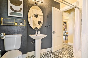 A bathroom with a toilet, sink, and mirror. There is a shelf with decorative items and a shower curtain. - Colorful El Paso Home w/ Deck & Mtn Views! (El Paso)