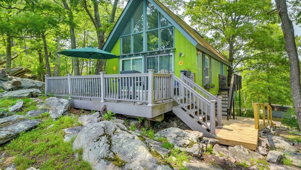 A cabin with a wooden deck, a covered outdoor seating area, and a staircase leading to a second level. - Great Cacapon Cabin w/ Mountain Views (Great Cacapon)