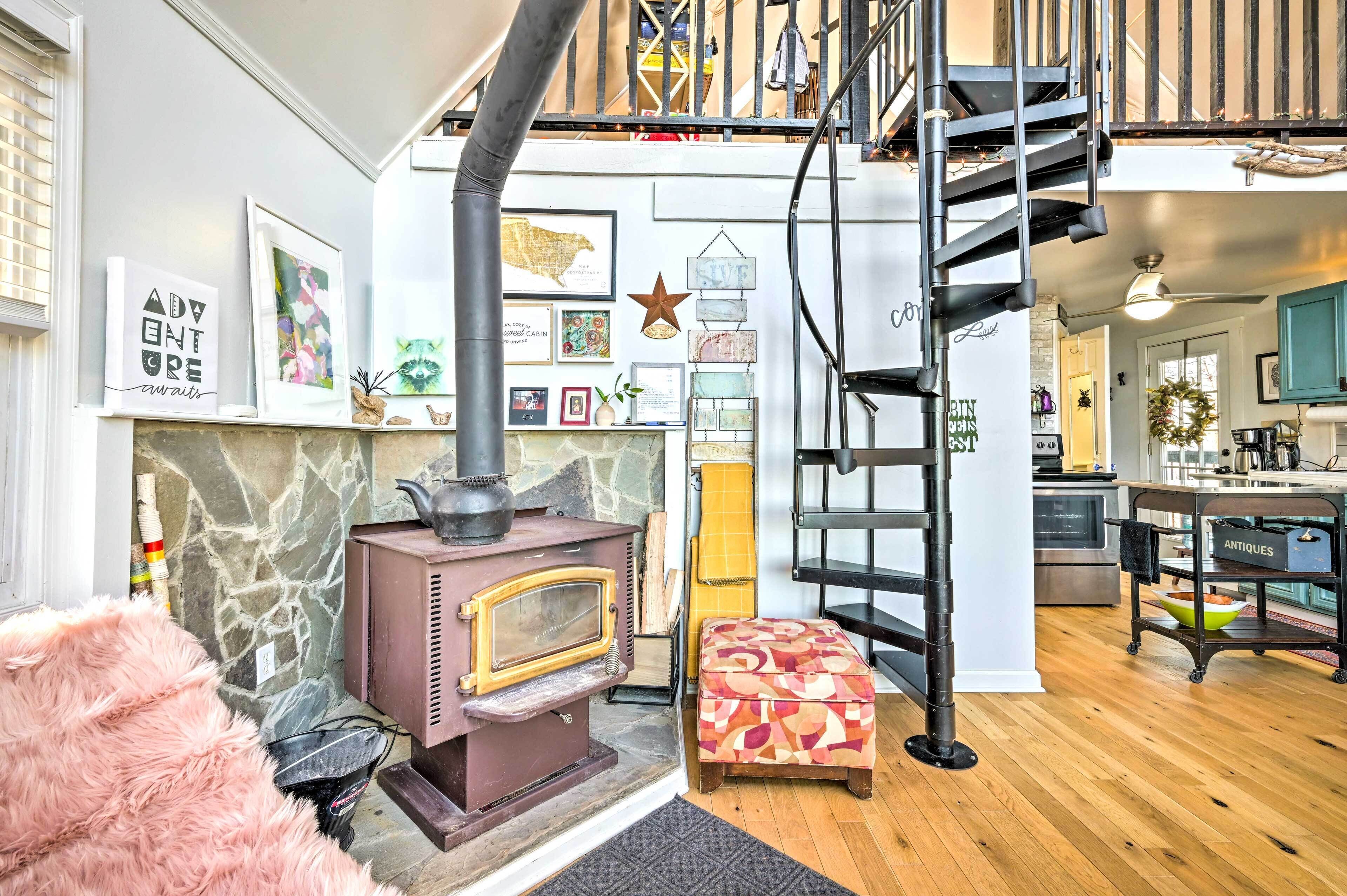 A cozy living room with a stone fireplace, a colorful ottoman, and a spiral staircase leading to an upper level.