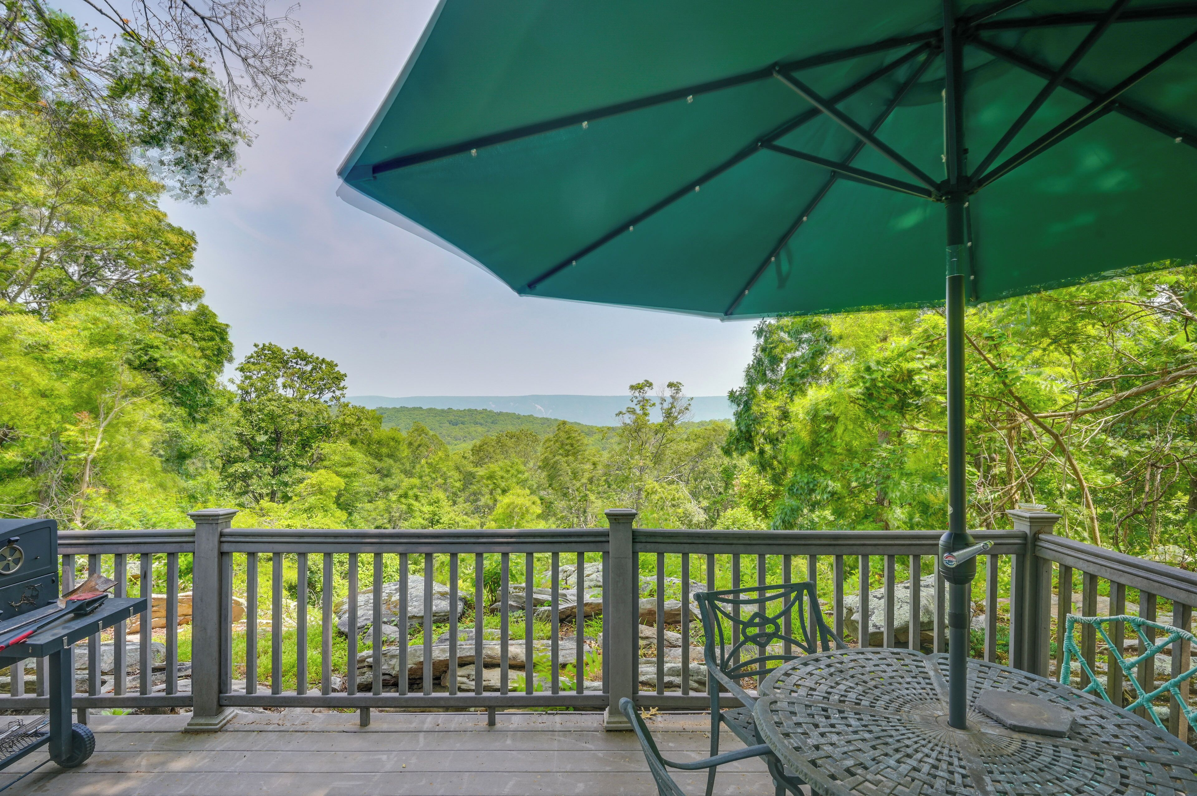 A patio with a green umbrella, metal railing, and a table with chairs.