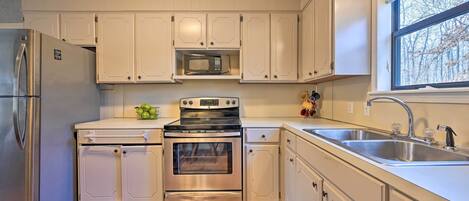 Una cocina con electrodomésticos de acero inoxidable, armarios blancos, un microondas, un horno y un lavamanos.