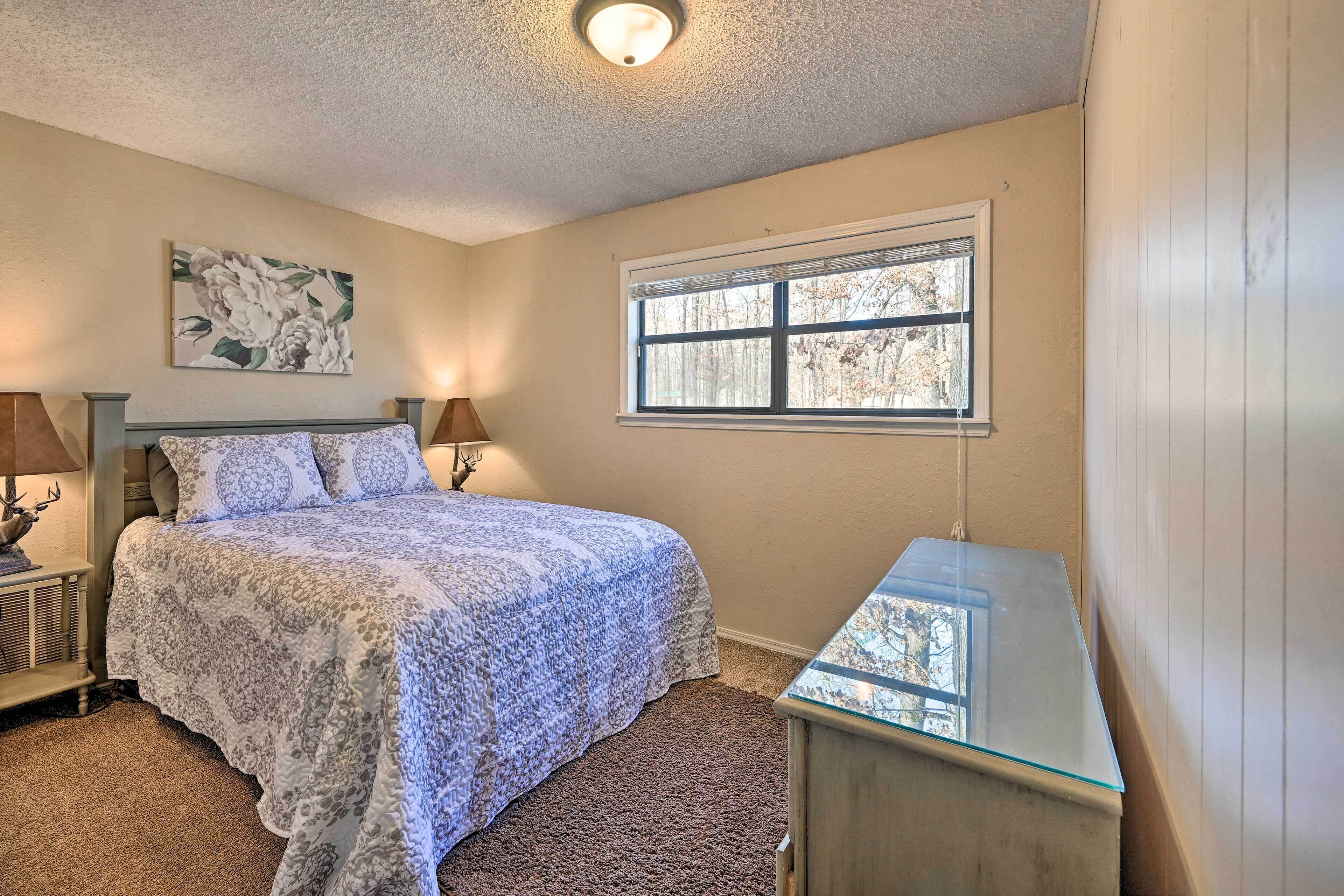 A bedroom with a bed, a nightstand, a lamp, a window, and a ceiling light.