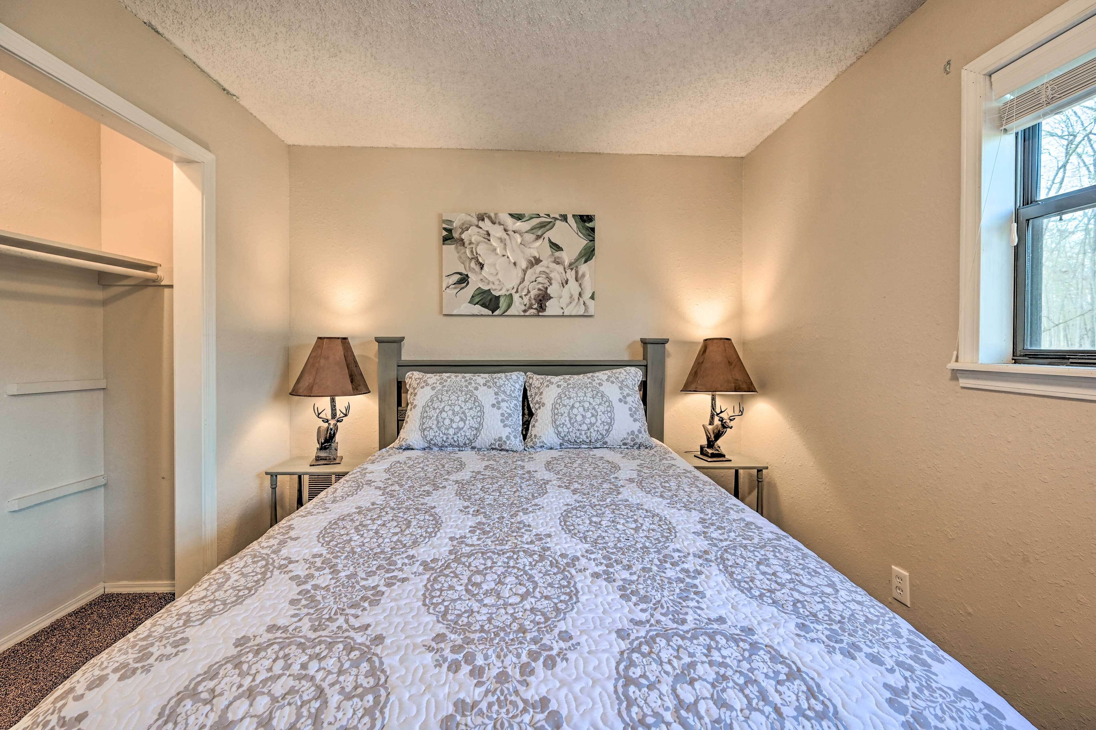 A bedroom with a large bed, two bedside lamps, a wall-mounted artwork, and a window.