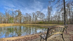 A park with a bench by a pond, surrounded by leaf-covered ground and trees. - 'hidden Oaks' Broken Bow Vacation Rental, Pets OK! (Broken Bow)
