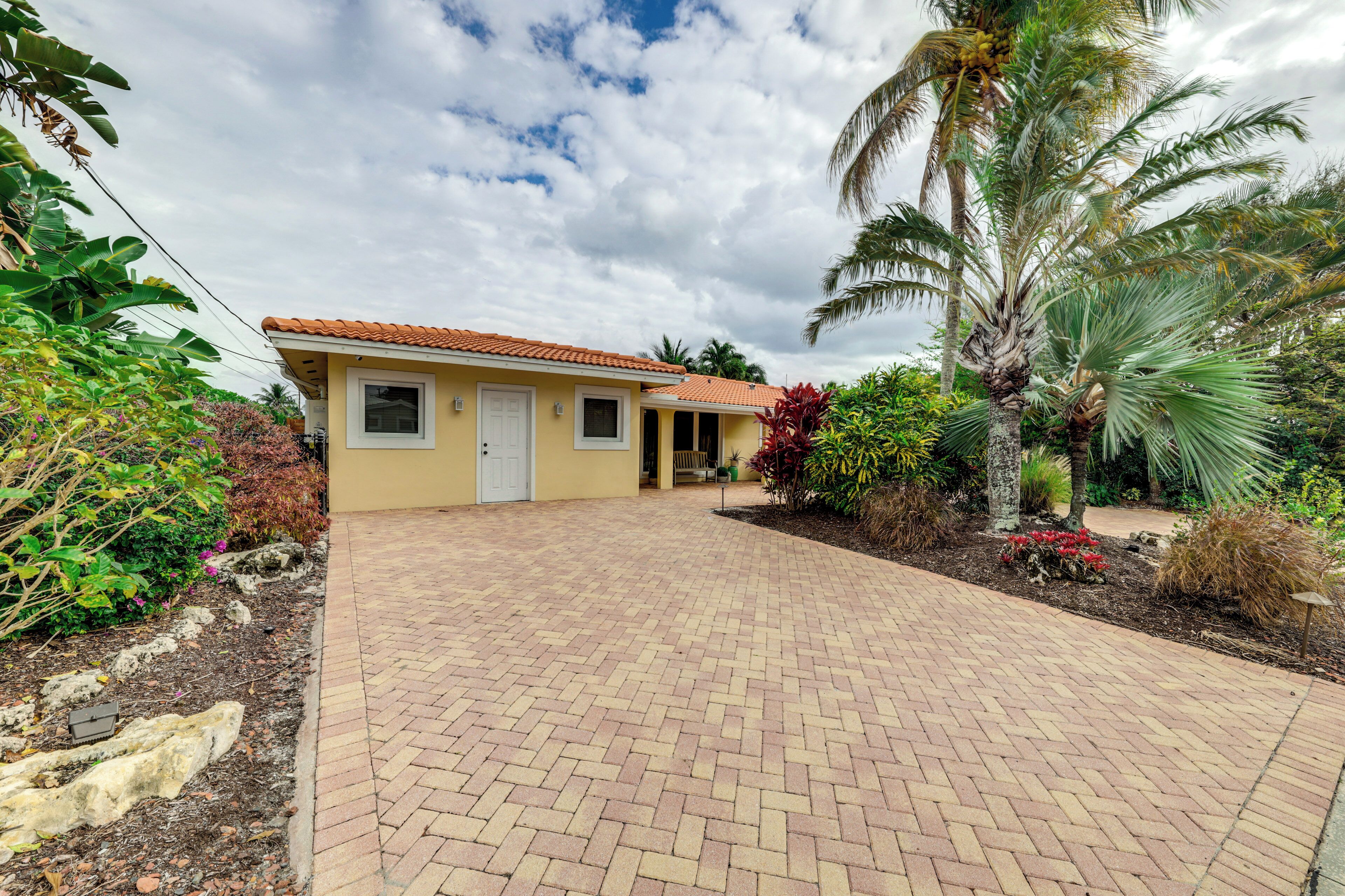 A yellow building with a tiled roof, a paved driveway, and surrounding tropical vegetation.