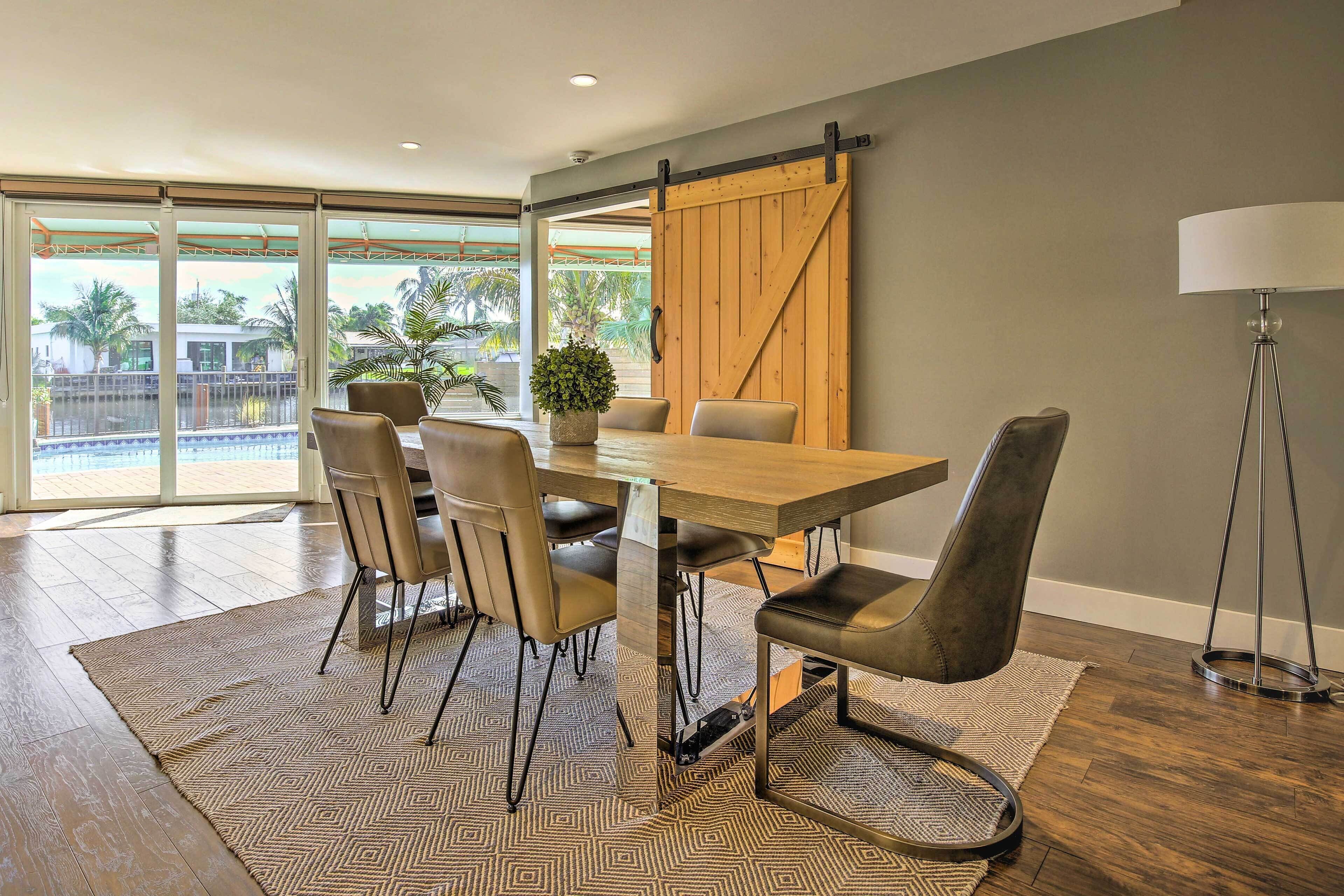 Un comedor con una mesa de madera, seis sillas, una planta en maceta y una puerta corredera estilo granero.