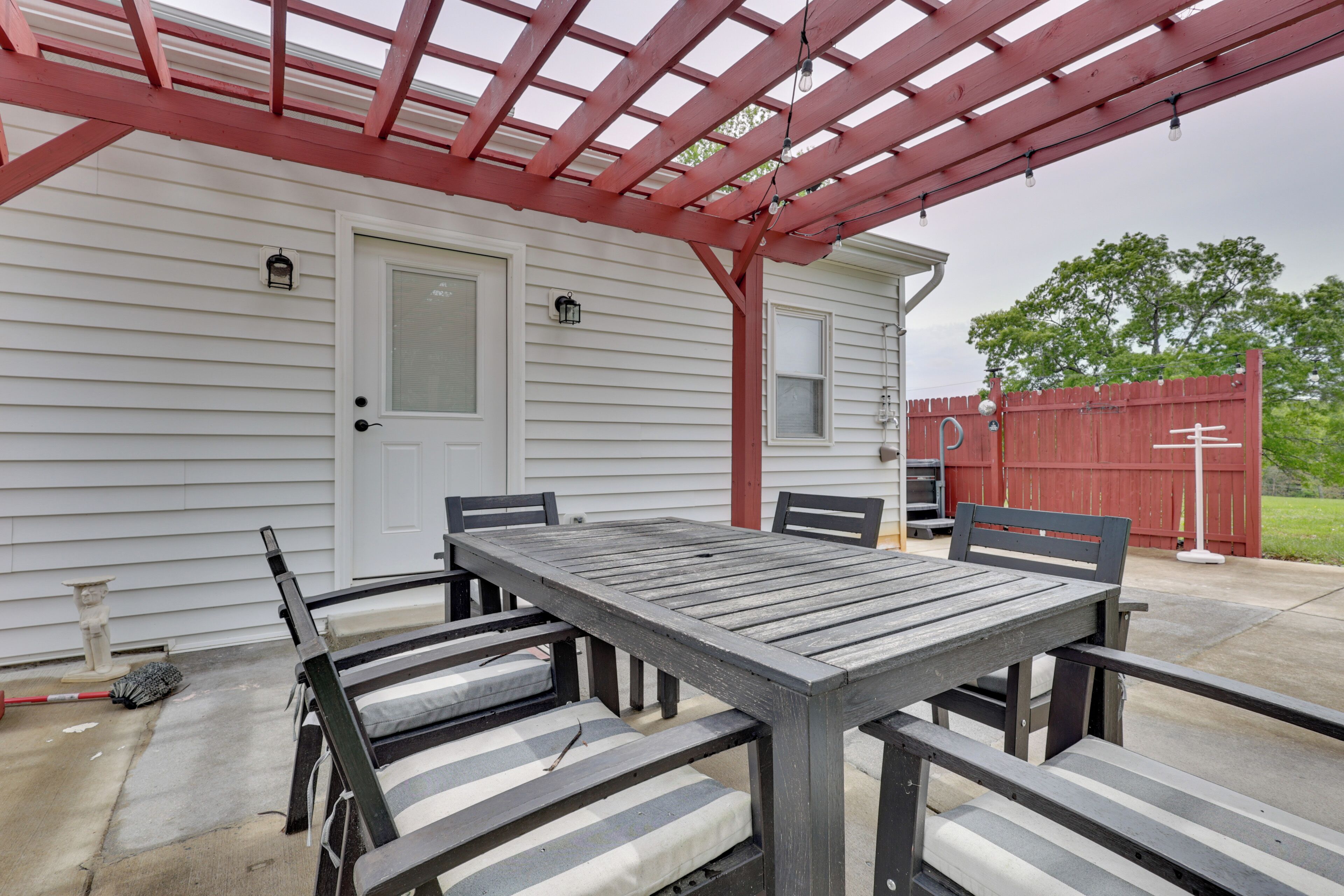 A covered patio with a table and chairs, a door, and a red fence in the background.