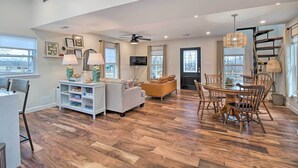 Una amplia sala de estar con piso de madera, un comedor con mesa y sillas de madera, un sofá y un ventilador de techo.