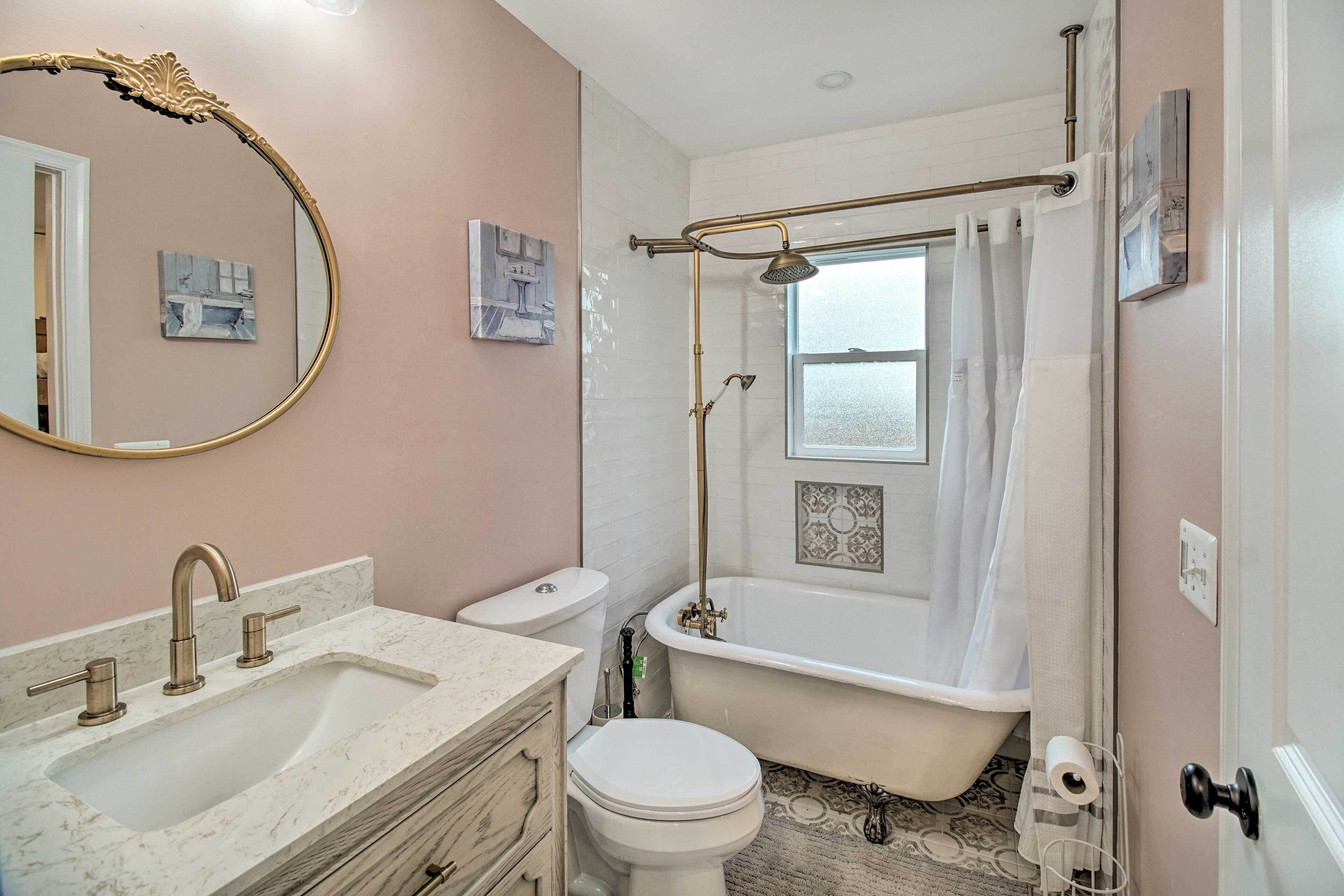 Une salle de bain avec un lavabo en marbre, des toilettes blanches, une baignoire avec pomme de douche et un grand miroir.