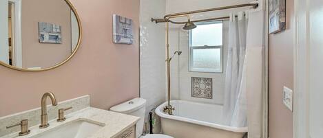 Un baño con lavamanos de mármol, inodoro blanco, bañera con cabezal de ducha y un espejo grande.