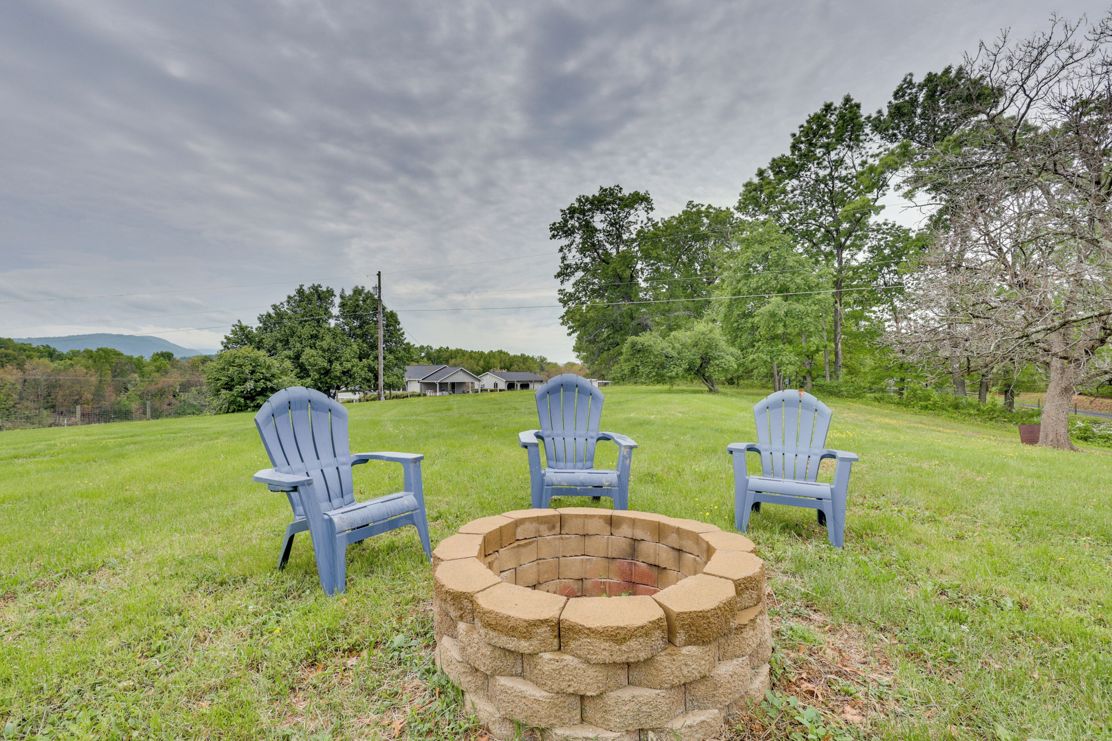 Un foyer en pierre, entouré de trois chaises Adirondack, se trouve dans un champ d’herbe.