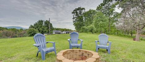 Un foyer en pierre, entouré de trois chaises Adirondack, se trouve dans un champ d’herbe.