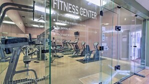 A fitness center with exercise equipment, glass walls, and a sign with rules.