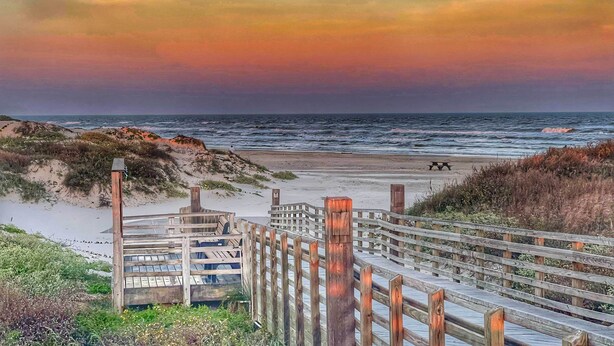 A wooden boardwalk leading to a beach with a wooden structure at the end.
